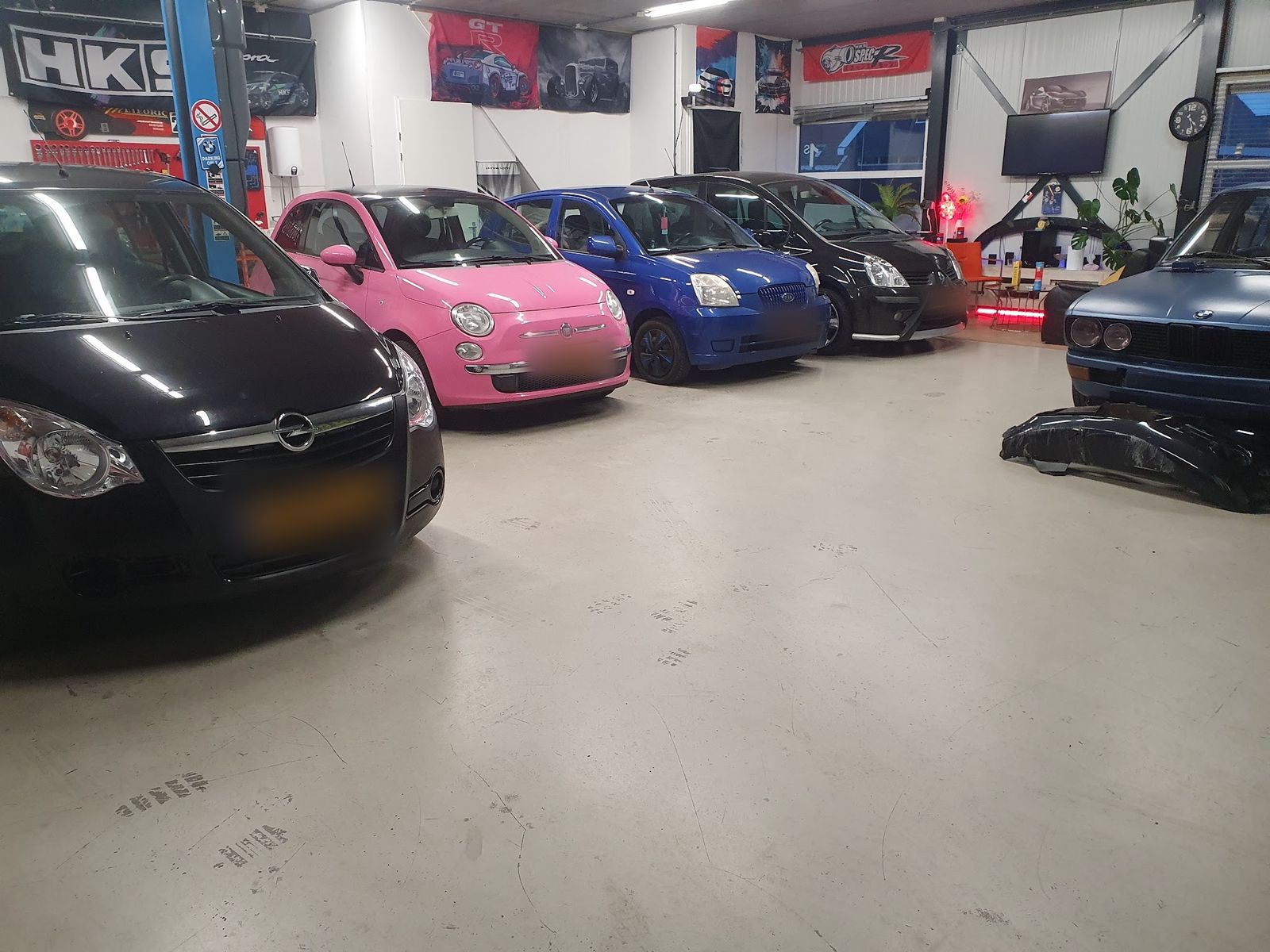 Een rij auto's in de hal, waaronder een roze Fiat 500 en een blauwe Kia