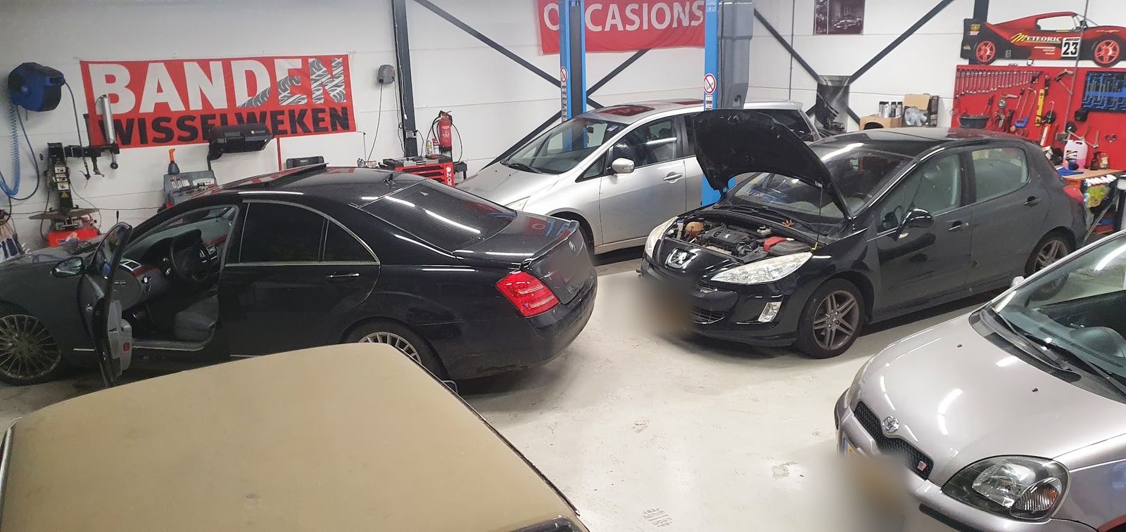 Drukke werkplaats met een Mercedes, een Peugeot met open motorkap en een Toyota